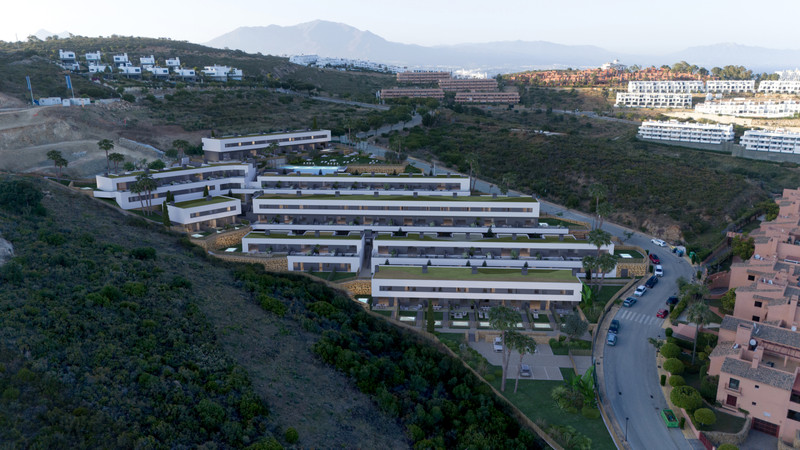 Blue Wave – Manilva - flyfoto av moderne hvitt boligkompleks terrassert inn i åssiden med grønne tak og basseng