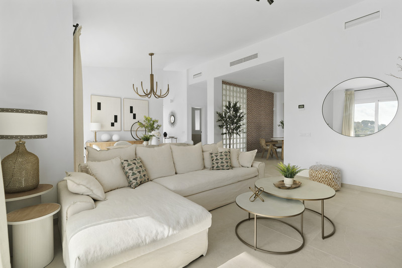 Urbanización Olimpo – Mijas - lyst åpent stue med kremfarget sofa, gullfargede sofabord og rundt speil