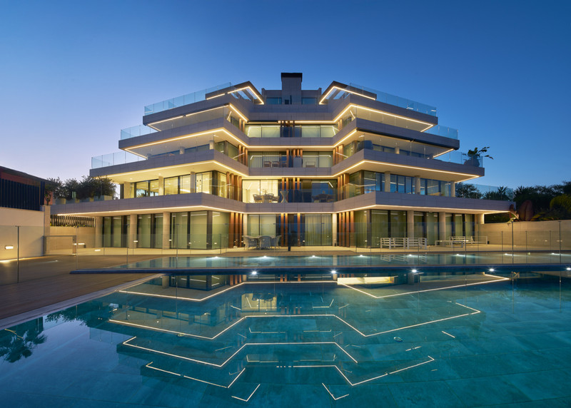 The Sapphire – Estepona - illuminated modern exterior facade with rooftop terraces and foreground swimming pool at dusk